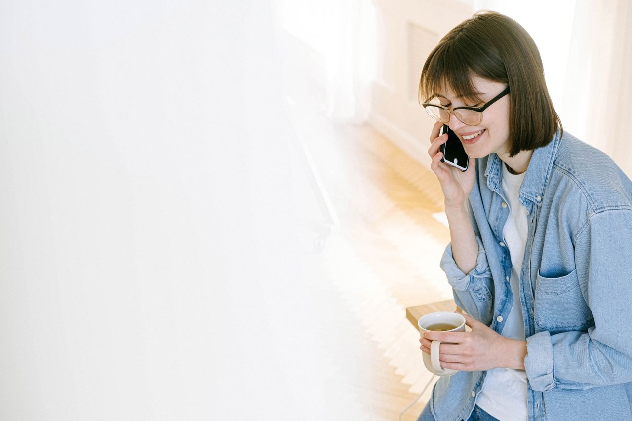 Femme souriante parlant au téléphone avec un café dans un intérieur lumineux.