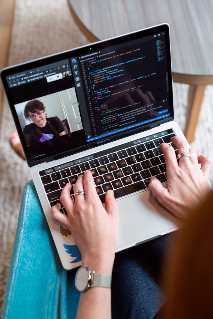 Personne en train de coder sur un ordinateur portable pendant une visioconférence, illustrant le travail à distance.